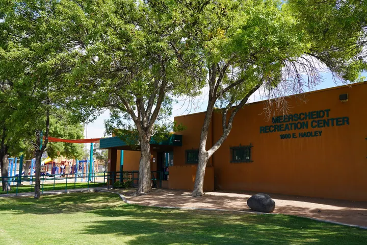 Exterior of Meerscheidt Recreation Center in Las Cruces, New Mexico, with trees and a playground visible beside the entrance.