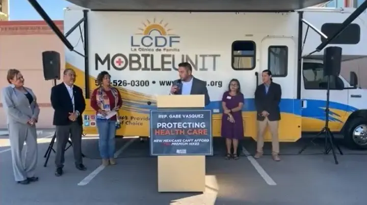 Rep. Gabe Vasquez speaks at a podium in front of La Clinica de Familia’s mobile health unit in Las Cruces.
