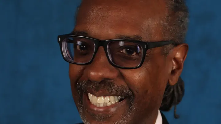 Close-up portrait of Gene Grant smiling against a blue background.