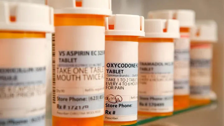 Several prescription pill bottles lined up on a shelf, including containers labeled for aspirin, oxycodone and tramadol.