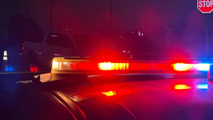 Police lights flash red and blue at night as law enforcement vehicles block a Las Cruces intersection during an active scene.