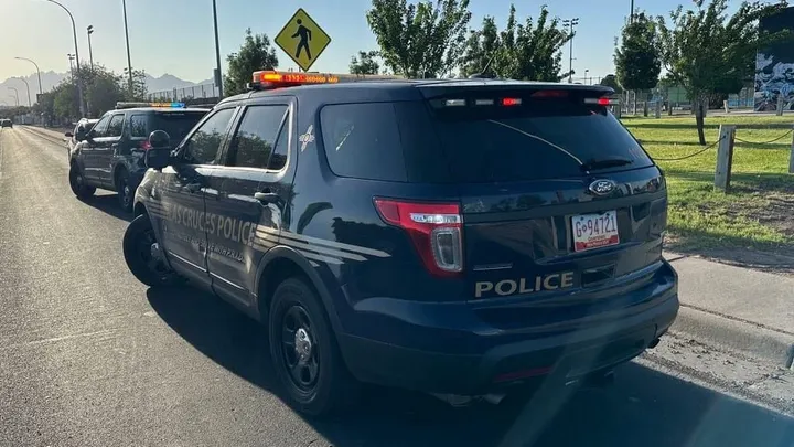 Las Cruces police vehicles parked along a city street with lights flashing near a pedestrian crossing.
