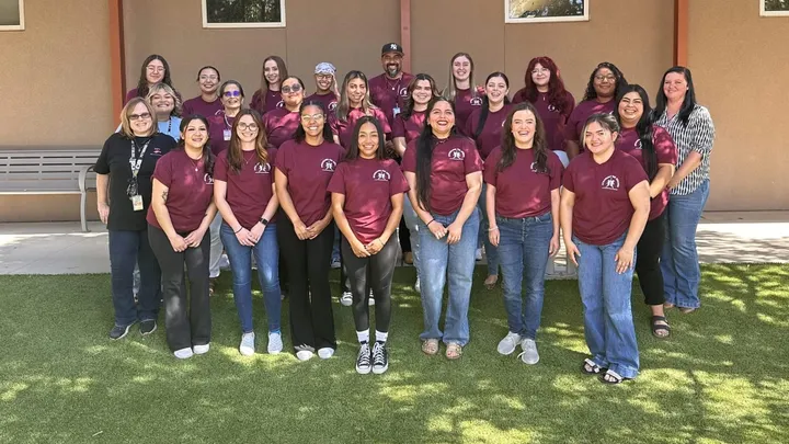 Group photo of NMSU social work students and Las Cruces Public Schools staff standing outside, many wearing matching maroon shirts.
