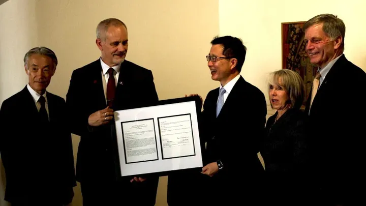 Five people stand together holding a framed document during a signing ceremony marking a new partnership between New Mexico State University and a Japanese technology company.