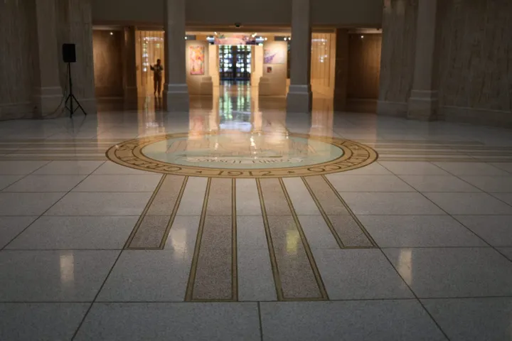 The New Mexico state seal is inlaid on the marble floor of the state Capitol in Santa Fe, with the Rotunda and art gallery visible in the background.