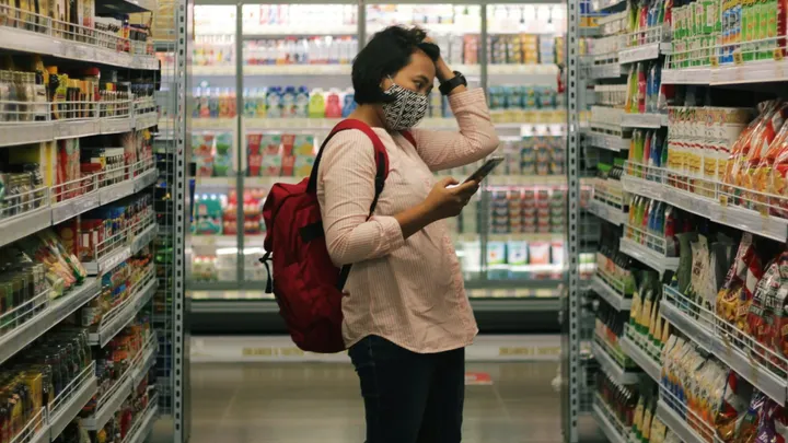 Shopper wearing a mask checks a shopping list while standing in a grocery aisle, reflecting cost and access concerns for New Mexico families.