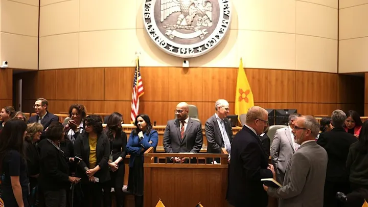 People gather and talk on the New Mexico House floor beneath the state seal and flags after the Nov. 10, 2025 special legislative session.