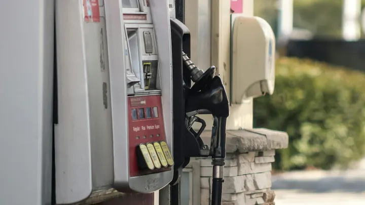 Close-up of a gas pump with a black fuel nozzle resting in its holder beside grade selection buttons at a service station.