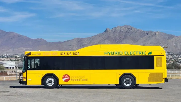A yellow South Central Regional Transit hybrid-electric bus parked outdoors with desert mountains in the background, displaying SCRTD branding and “Hybrid Electric” along the roofline.