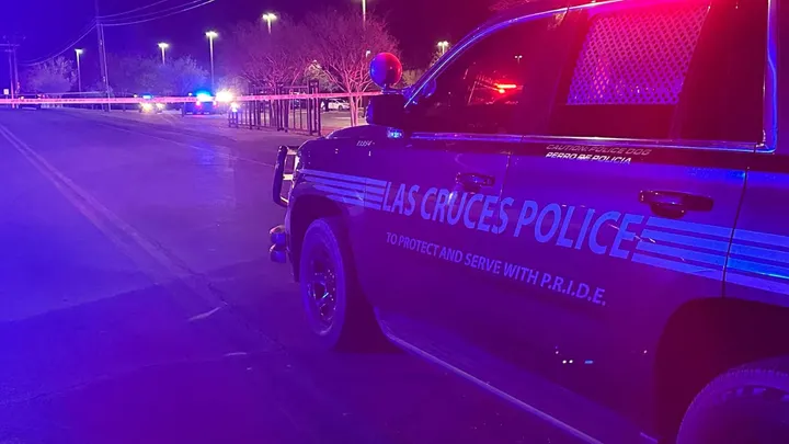 Las Cruces Police vehicle blocks a roadway at night as officers investigate a crash, with police tape stretched across the street and emergency lights illuminating the scene.