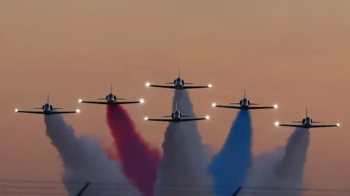 Six jets fly in tight formation at dusk, releasing red, white and blue smoke during an aerial demonstration ahead of Holloman Air Force Base’s 2026 air show.