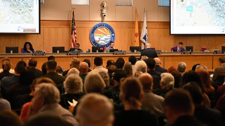 Residents fill the Doña Ana County Commission chambers as officials discuss Project Jupiter during a public meeting, with maps displayed on screens at the front of the room.