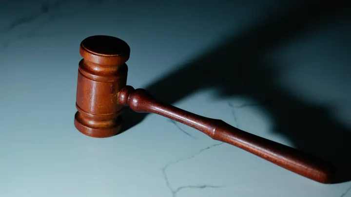 A wooden judge’s gavel rests on a light-colored surface, casting a shadow under directional lighting.