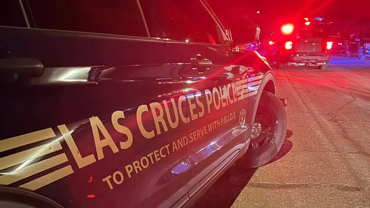 Las Cruces police vehicle parked on a roadway at night with red and blue emergency lights flashing from multiple police units in the background.