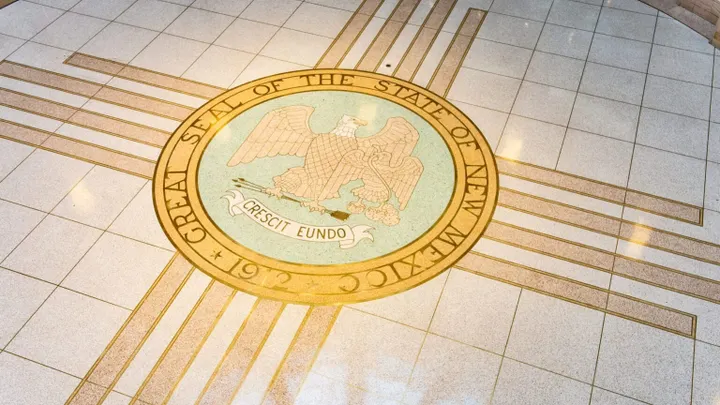 Mosaic of the Great Seal of the State of New Mexico on a tiled floor, showing the eagle, Zia sun symbol rays, the motto “Crescit eundo” and the year 1912.