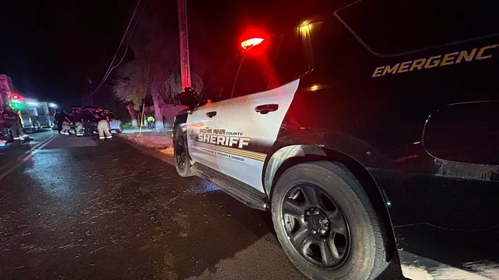 Doña Ana County Sheriff’s Office vehicle parked on a dark roadway at night with emergency lights flashing as firefighters and deputies respond to a scene in the background.