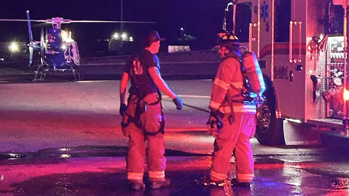 Emergency responders stand beside a fire truck while a helicopter sits nearby during a nighttime response scene.