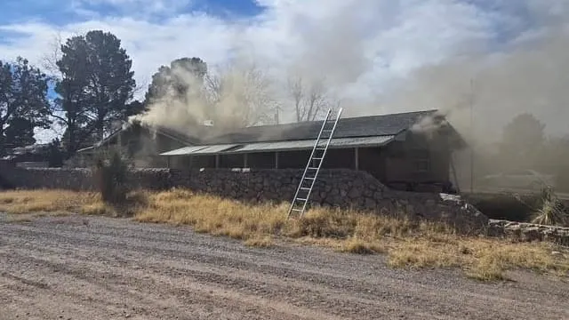 Firefighters respond to a residential structure fire on Cedardale Drive in Las Cruces, with smoke visible coming from the roof and a ladder positioned against the home.