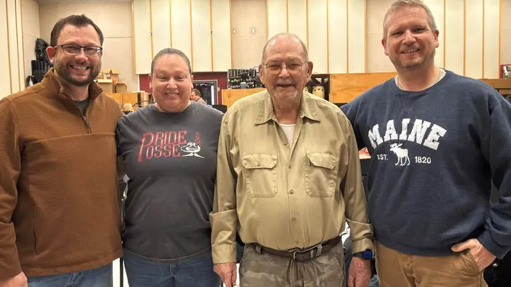 Rod Pior, Karen Padilla, Jim Young and Dr. Michael Mapp stand together in the NMSU band room, smiling in front of music stands and percussion instruments.