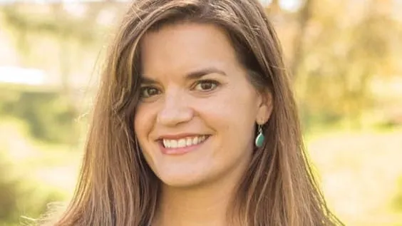 New Mexico Secretary of State Maggie Toulouse Oliver smiles in an outdoor portrait with greenery in the background.