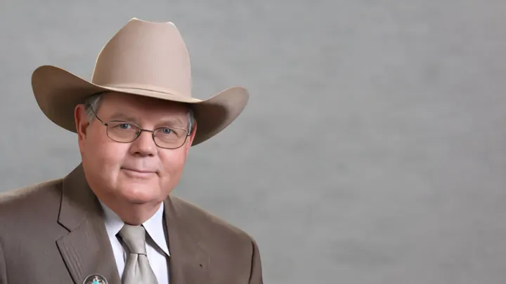 Portrait of New Mexico State Sen. Pat Woods wearing a cowboy hat and suit against a gray background.
