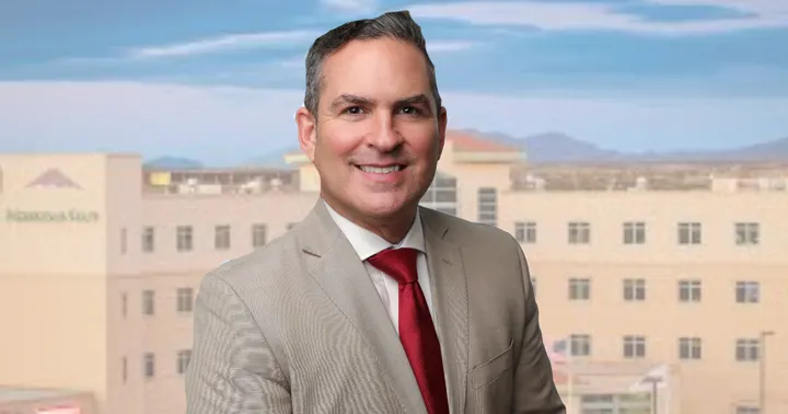 Portrait of MountainView Regional Medical Center CEO Patrick Shannon in a tan suit and red tie, with the hospital campus blurred in the background.