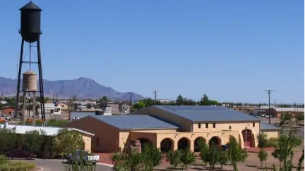 Pancho Villa State Park Exhibition Hall in Columbus, New Mexico, with historic water tower and desert mountains in the background.