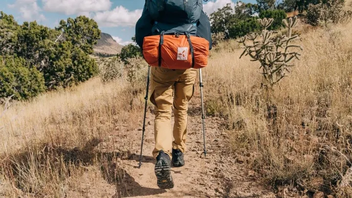 Hiker with backpack walking along a trail in a New Mexico desert landscape.