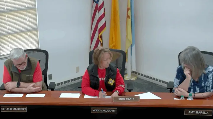 Otero County commissioners sit at a dais during a public meeting, with nameplates visible and state and U.S. flags behind them.
