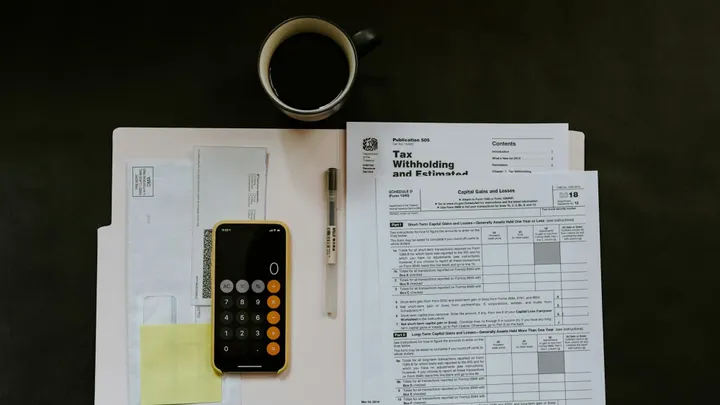 Tax documents, envelopes and a calculator sit on a desk next to a cup of coffee.