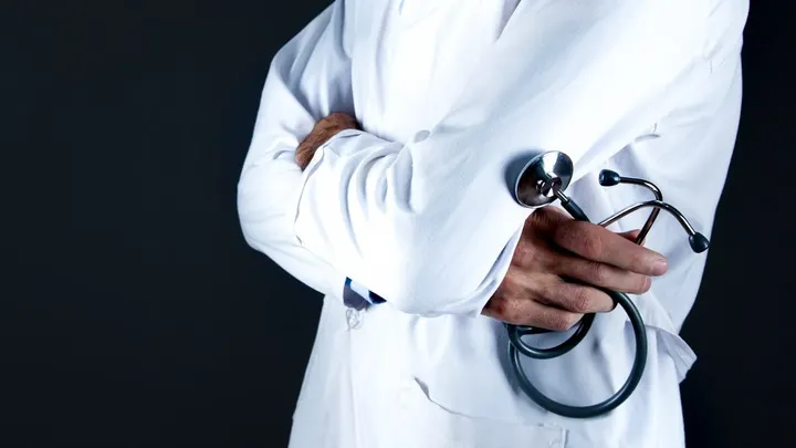 A doctor in a white coat holds a stethoscope, representing health care workforce shortages