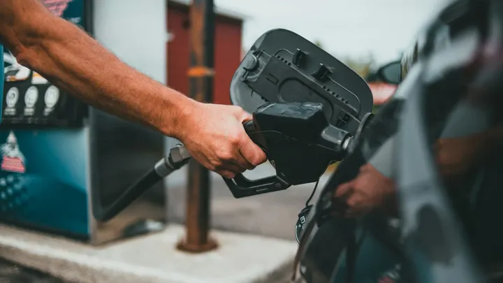 Person pumping gasoline into a car at a gas station as fuel prices rise ahead of Spring Break travel.