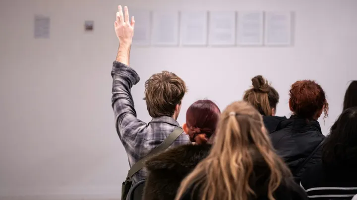 Person raises hand during in-person auction registration or bidding event with attendees seated in a room