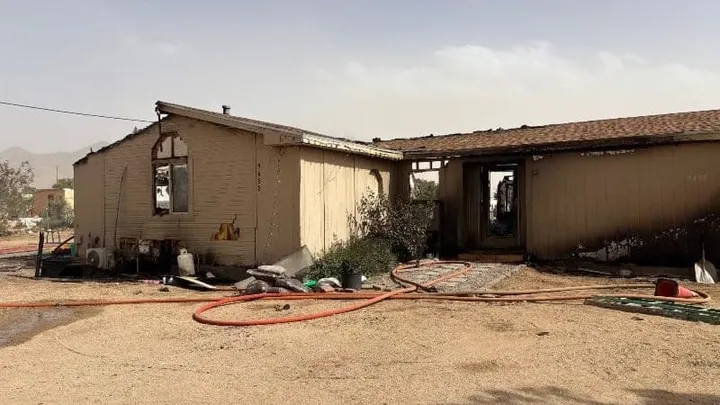 Single-story home on Hondo Road with visible fire damage, hoses on the ground, and burn marks around windows and exterior walls.