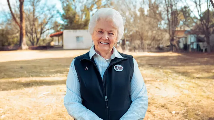 Wanda Bowman stands outdoors smiling in a yard, wearing a vest and collared shirt.