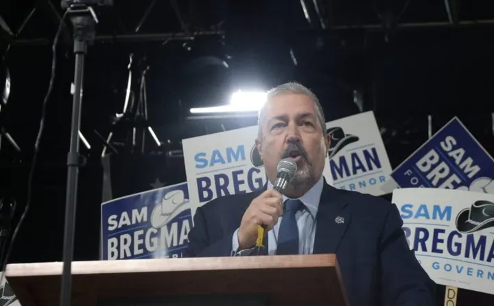Sam Bregman speaks at a campaign event while supporters hold “Sam Bregman for Governor” signs behind him.