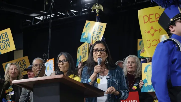 Deb Haaland speaks at a campaign event while supporters hold “Deb for Gov” signs in the background.