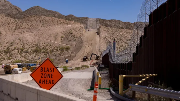 Construction equipment works near a “Blast Zone Ahead” sign along a section of the border wall at Mount Cristo Rey.