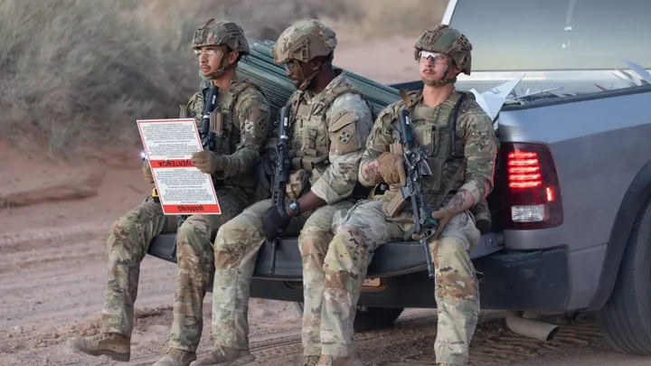 U.S. soldiers sit on the back of a truck holding a warning sign marking the boundary of a militarized border zone in southern New Mexico.