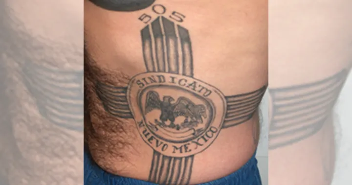 Close-up of a torso tattoo associated with the Syndicato de Nuevo Mexico prison gang, featuring a central emblem with “Sindicato Nuevo Mexico” text.