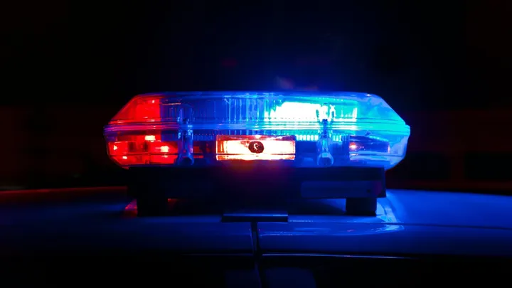 Red and blue emergency lights flash on top of a police vehicle at night.