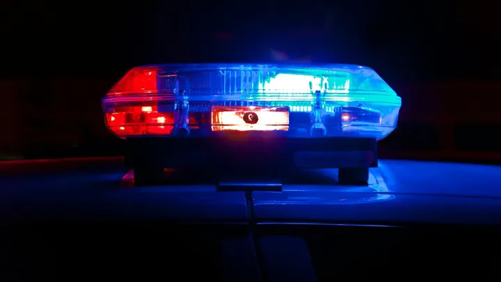 Red and blue emergency lights flash on top of a police vehicle at night.