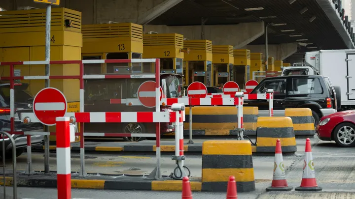 Toll booths with cars and barriers at a highway toll plaza, illustrating a toll road setting