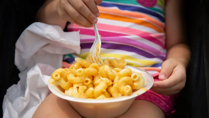 Child eating macaroni and cheese from a bowl, illustrating childhood nutrition and obesity trends
