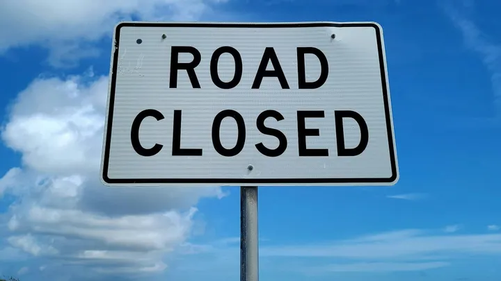 Road closed sign against a blue sky, indicating a traffic closure.