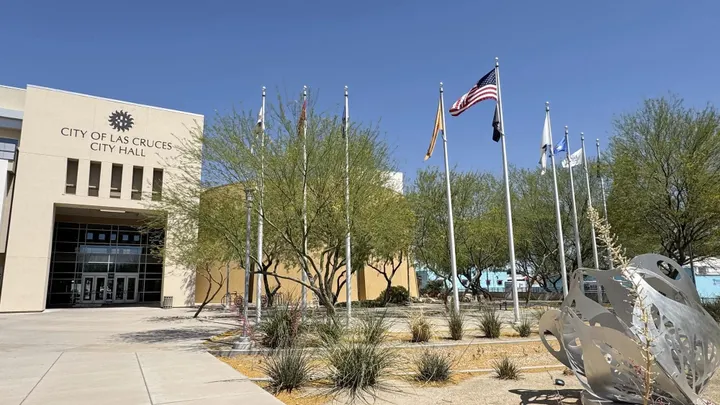Exterior view of Las Cruces City Hall with flags, desert landscaping and public art outside the building.
