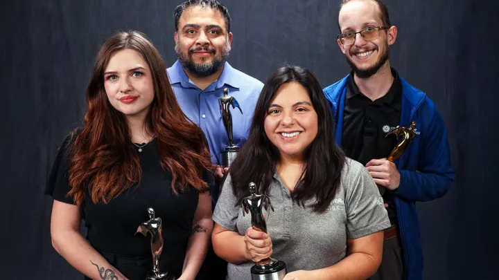 Four City of Las Cruces and Visit Las Cruces staff members pose with Telly Awards against a dark backdrop.