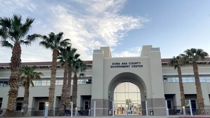 The Doña Ana County Government Center building is shown with palm trees lining the entrance.