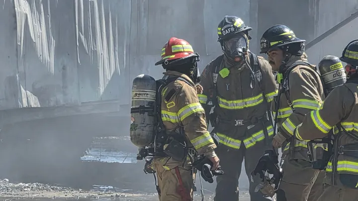 Doña Ana Fire Rescue firefighters wearing protective gear and air tanks stand near a smoke-damaged mobile home after a fire in Anthony.