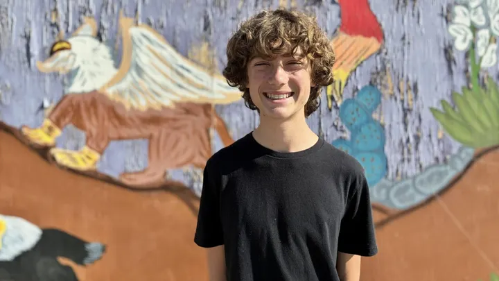 Mesilla Valley Leadership Academy student Adam Cram stands smiling in front of a colorful mural.